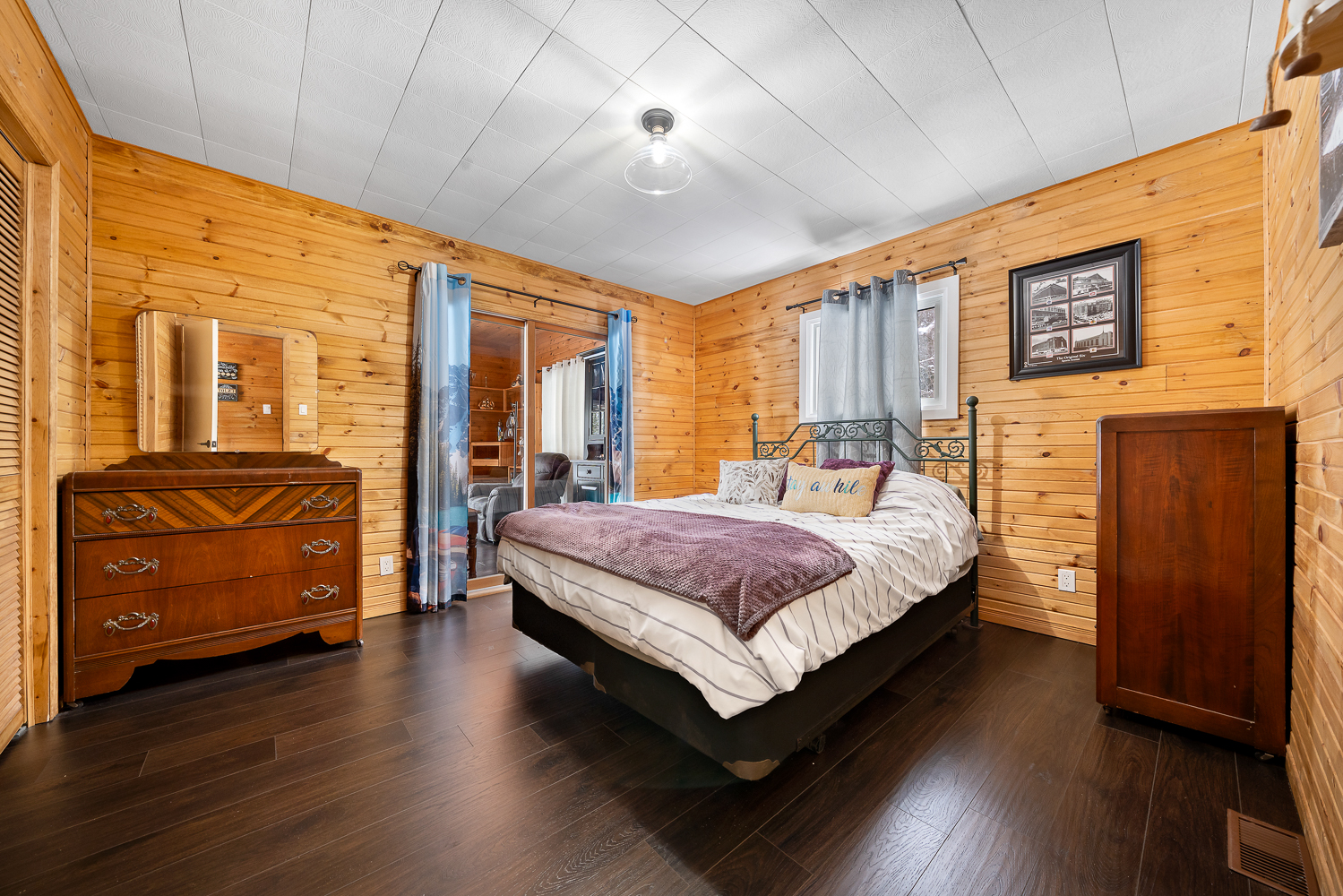 A white bed with a purple throw blanket in a wood-clad bedroom