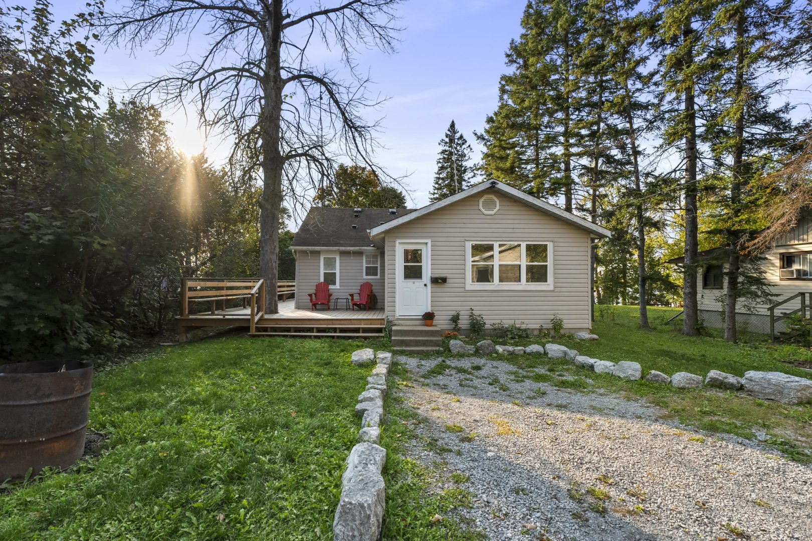 A beige clapboard cottage with a gravel driveway