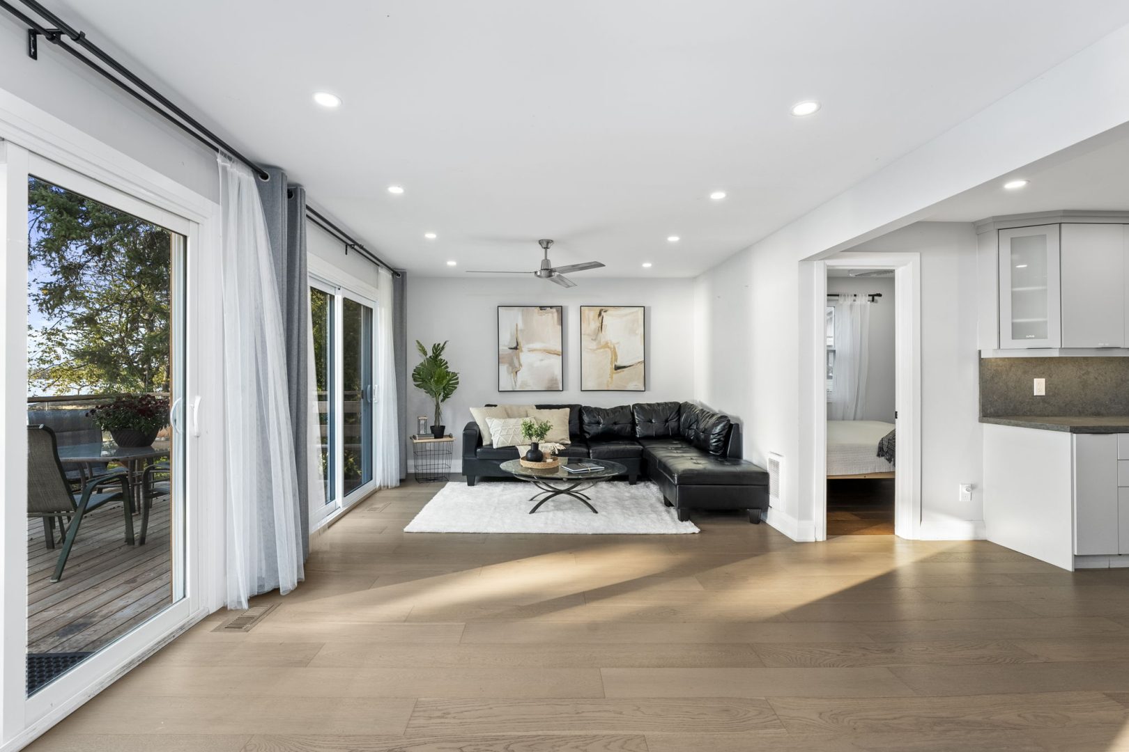 An L-shaped black leather couch in a white living area next to large sliding glass doors