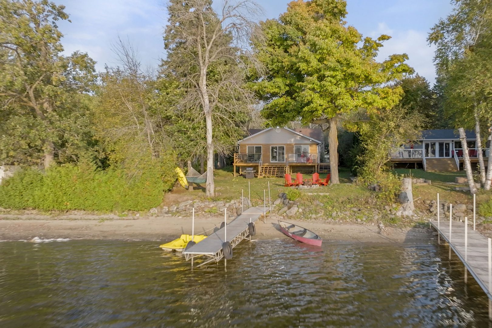 A beige clapboard cottage tucked away behind trees on a waterfront property