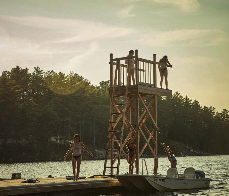Kids getting ready to jump into a lake from a wooden dive tower