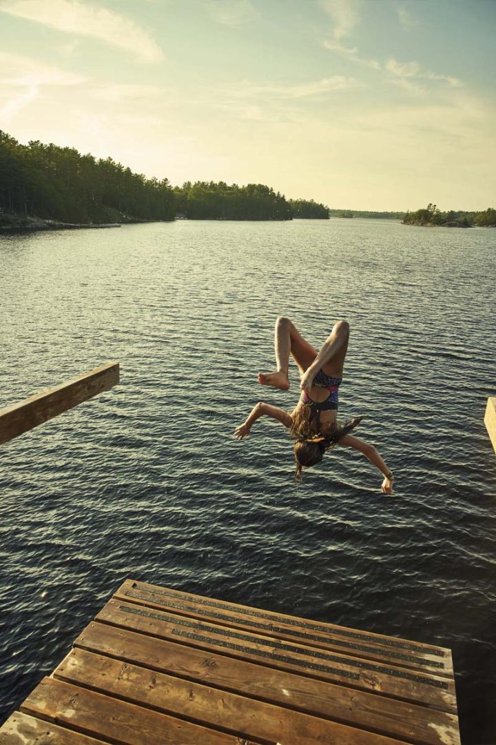 A girl diving backward into the water from the dock.