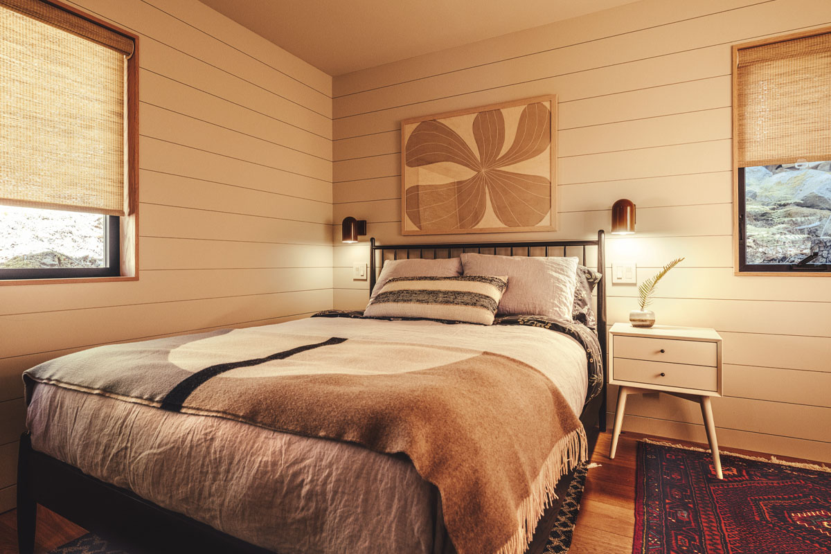 Bed with a beige and brown blankets and pillows, and a beige floral painting on the wall