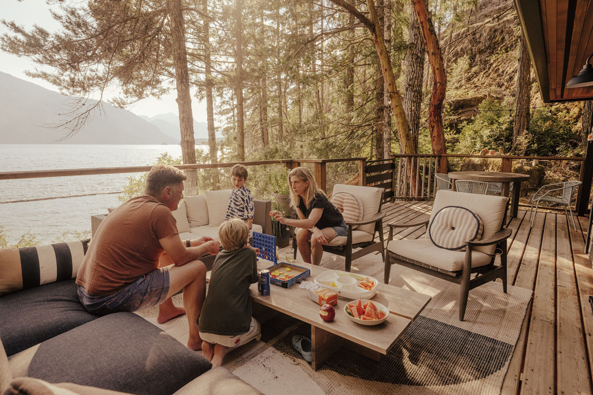 Family sitting on beige furniture on the terrace of their home, playing Connect 4 on the table
