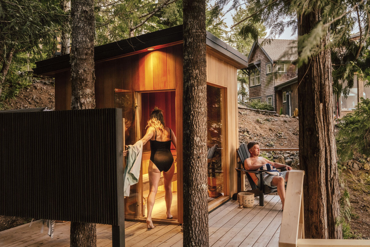 A woman walking into a sauna while her partner lounges on the chair right outside of it