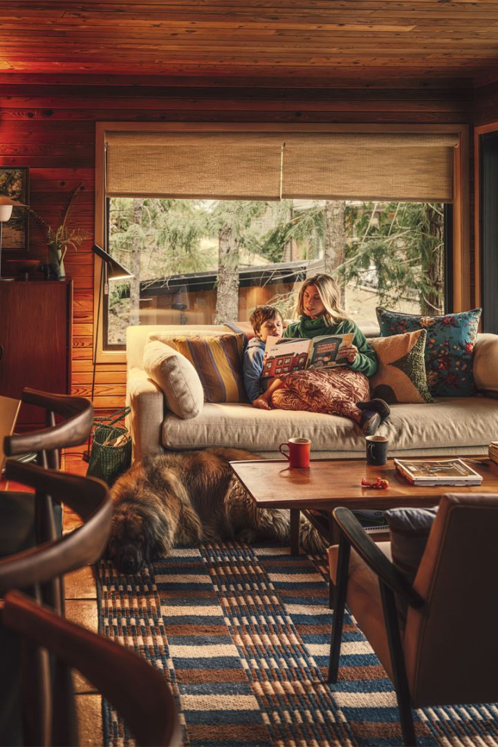 A mother reading a book to her son sitting on a beige couch with assorted coloured pillows
