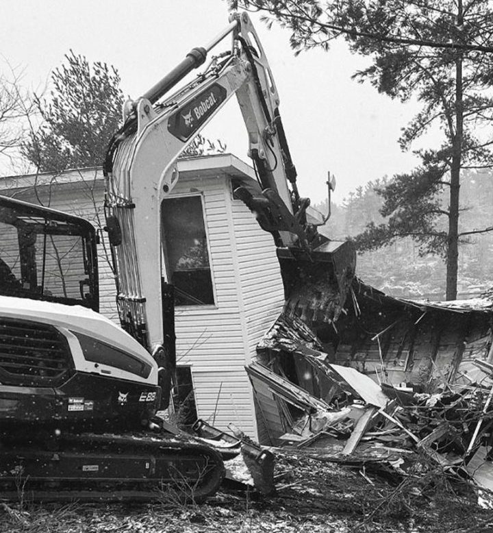 A cottage being demolished by an excavator