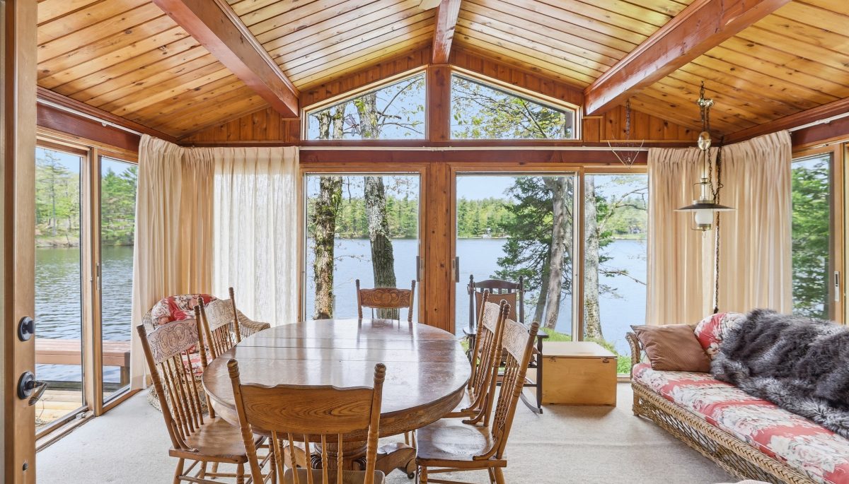 A wood dining table in a sunroom facing the lake