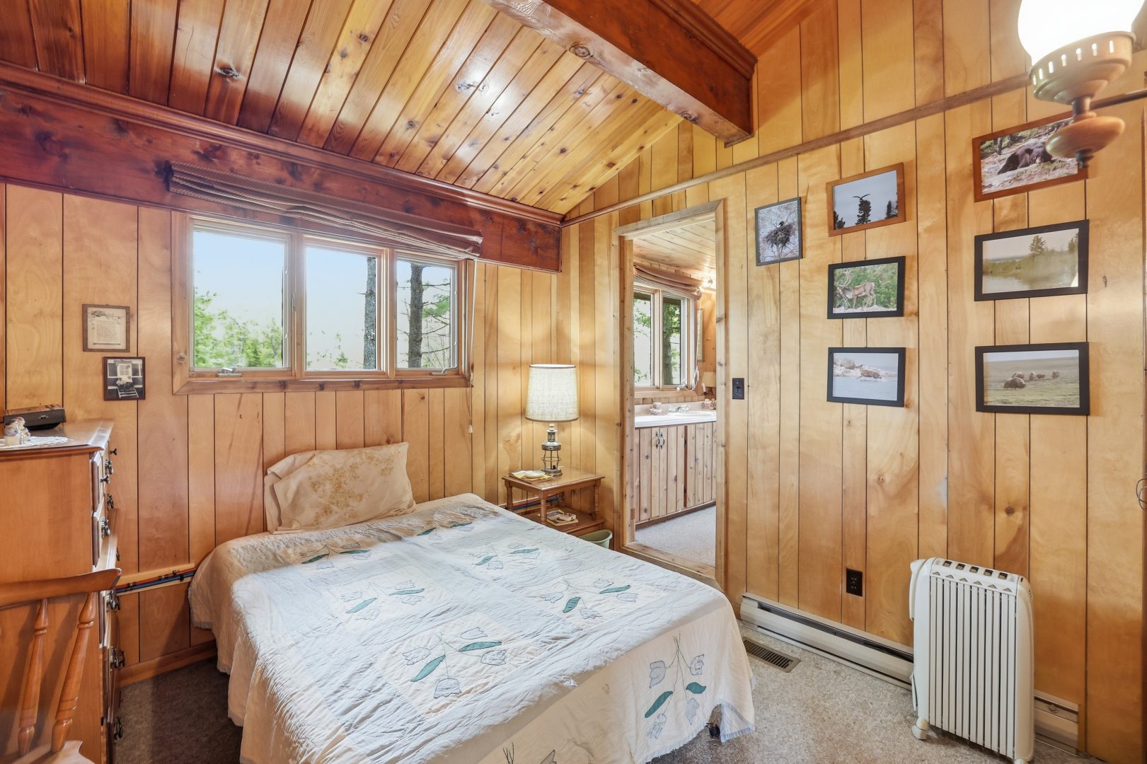 A white bed in a wood paneled room with an open doorway to the right