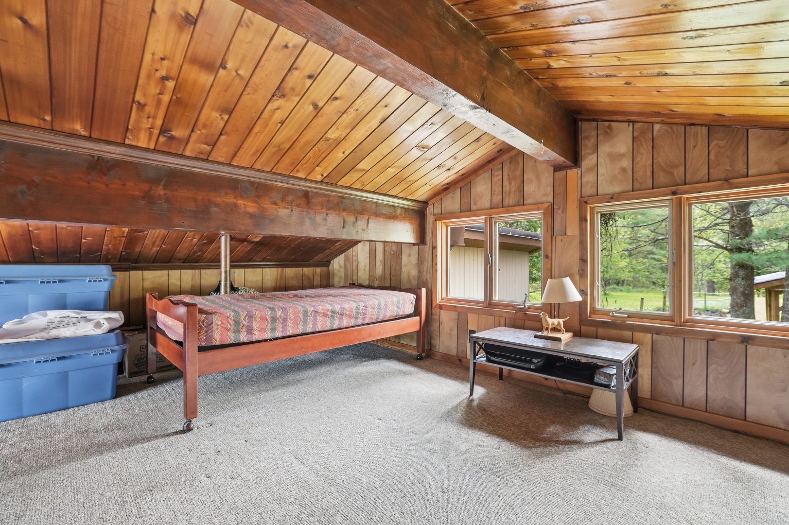 A wood-paneled loft with a small bed with plaid bedding