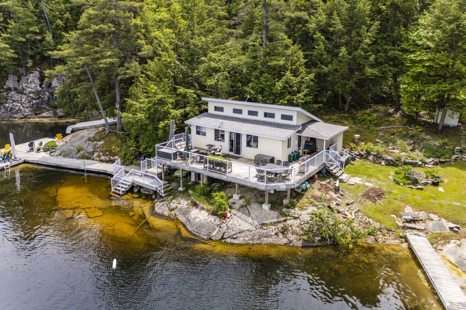 A white cottage with a large deck on a forested waterfront property