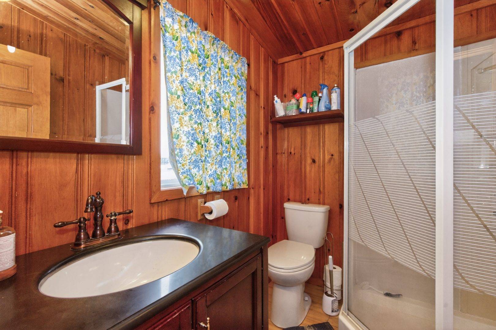 A wood paneled bathroom with a dark wood vanity and glass walk-in shower