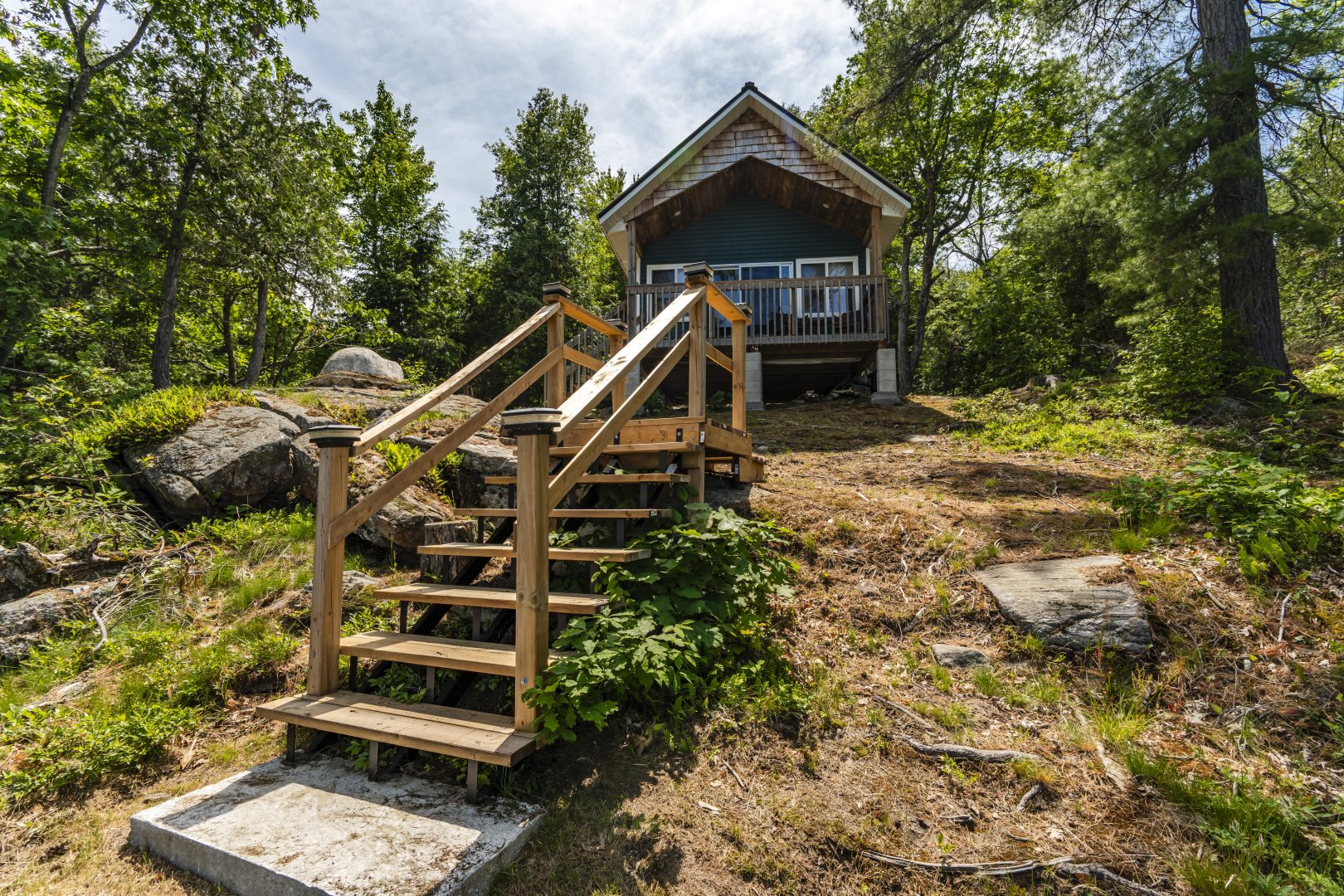 A green bunkie with wood steps leading up to the entrance