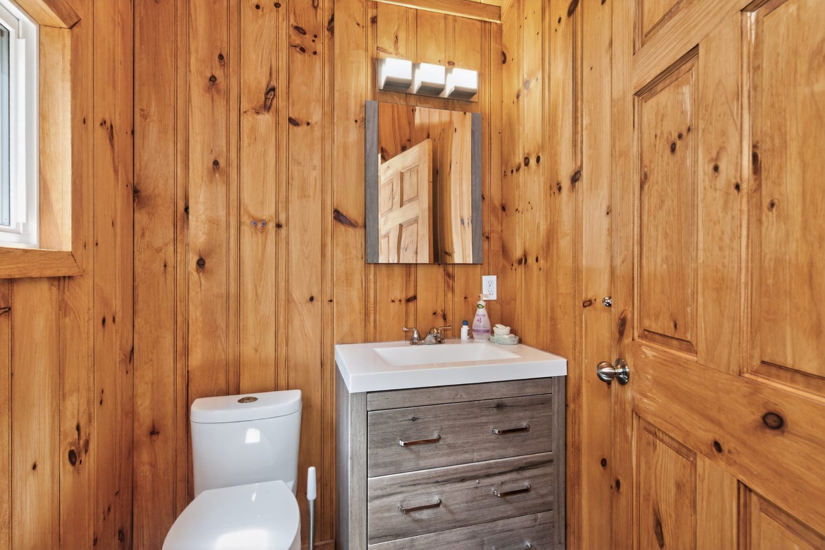 A toilet next to a grey wood vanity in a wood-paneled room