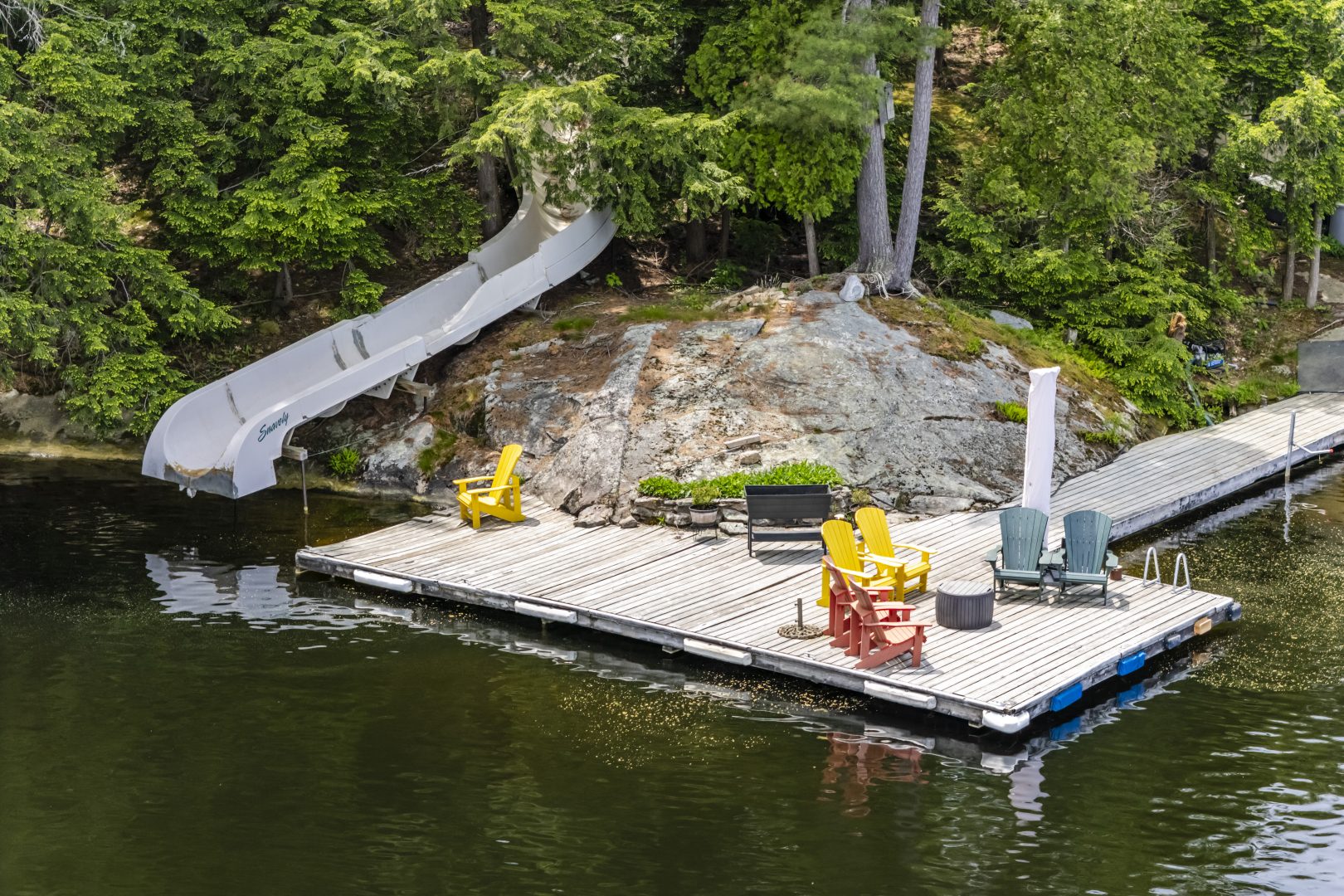 A dock with Muskoka chairs next to a waterslide