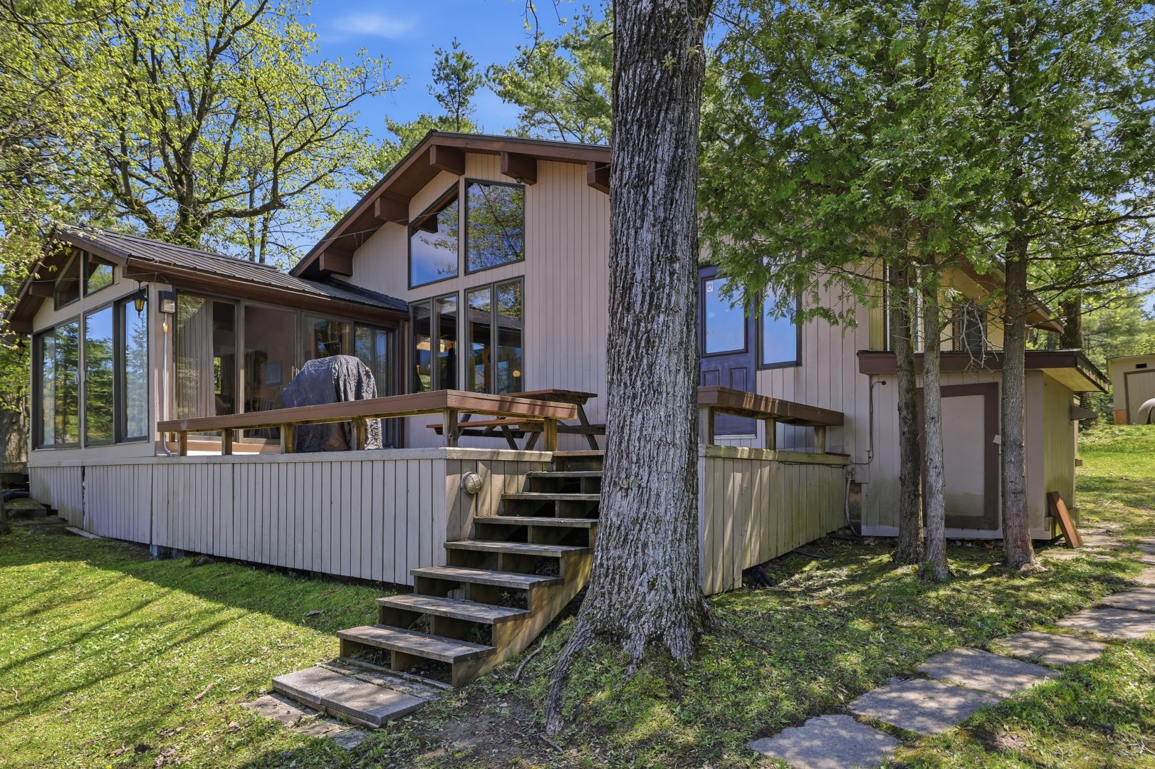 A beige cottage with a deck and steps leading down to the lawn