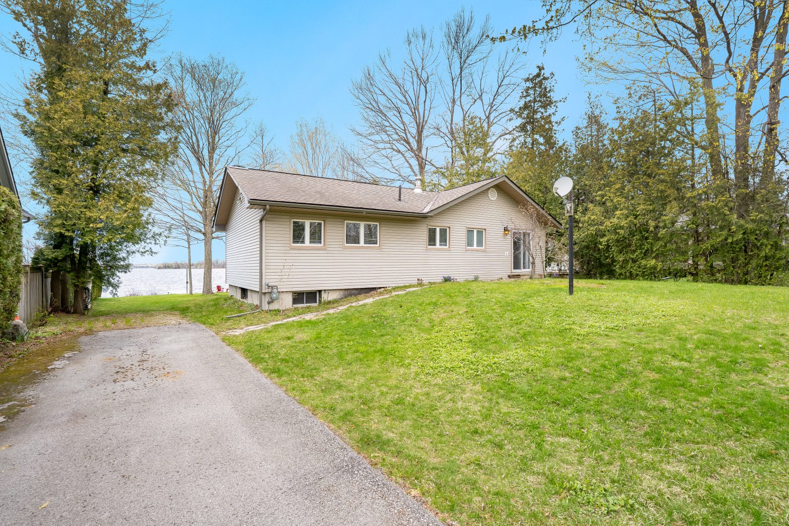 A beige clapboard cottage with a paved driveway next to a grassy lawn