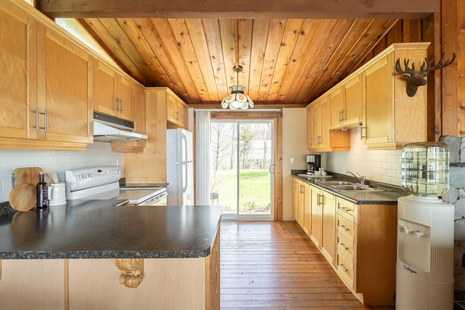 A wood-paneled kitchen with grey countertops facing sliding glass doors