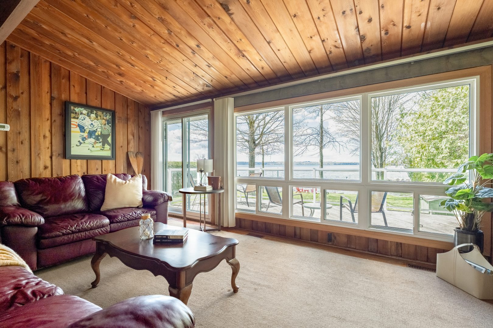 A burgundy leather couch and wood coffee table in a wood-clad room face a wall of windows