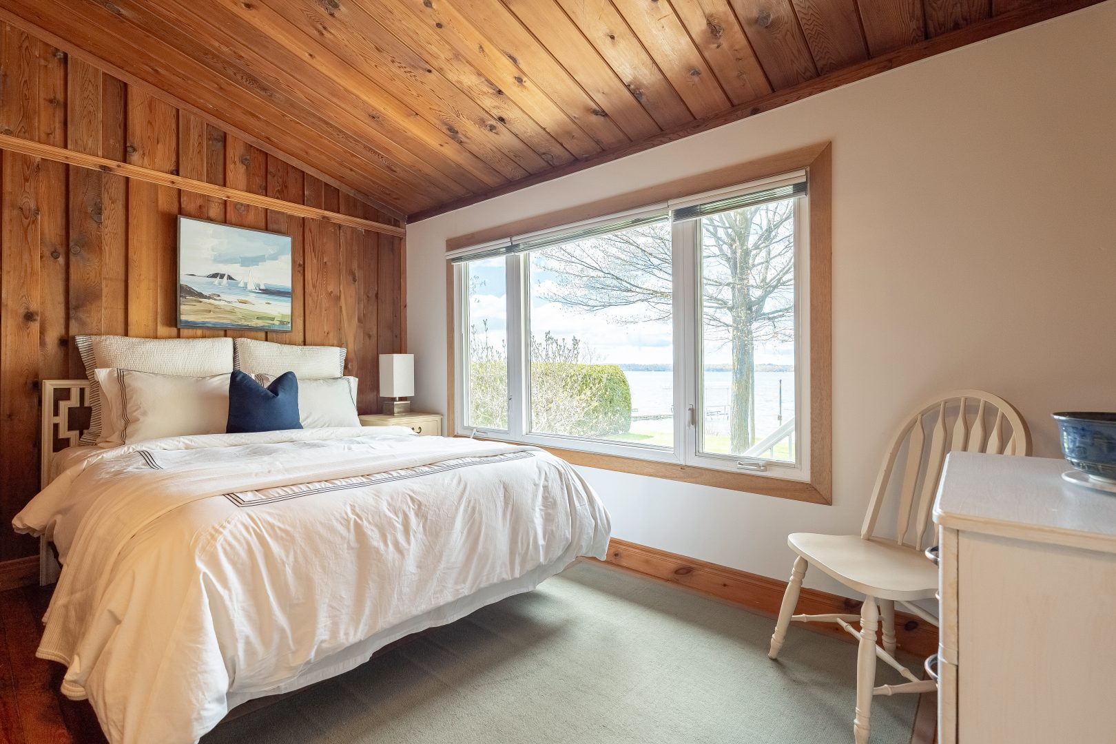 A white bed in a white and wood-clad bedroom with a large lake-facing window