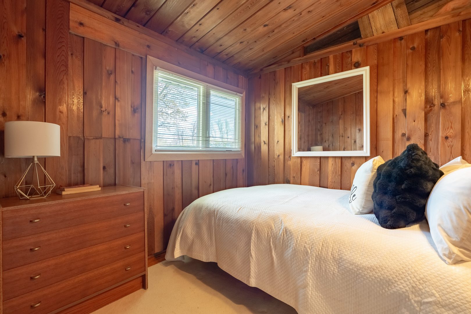 A white bed pressed against the wall in a dark wood-paneled bedroom