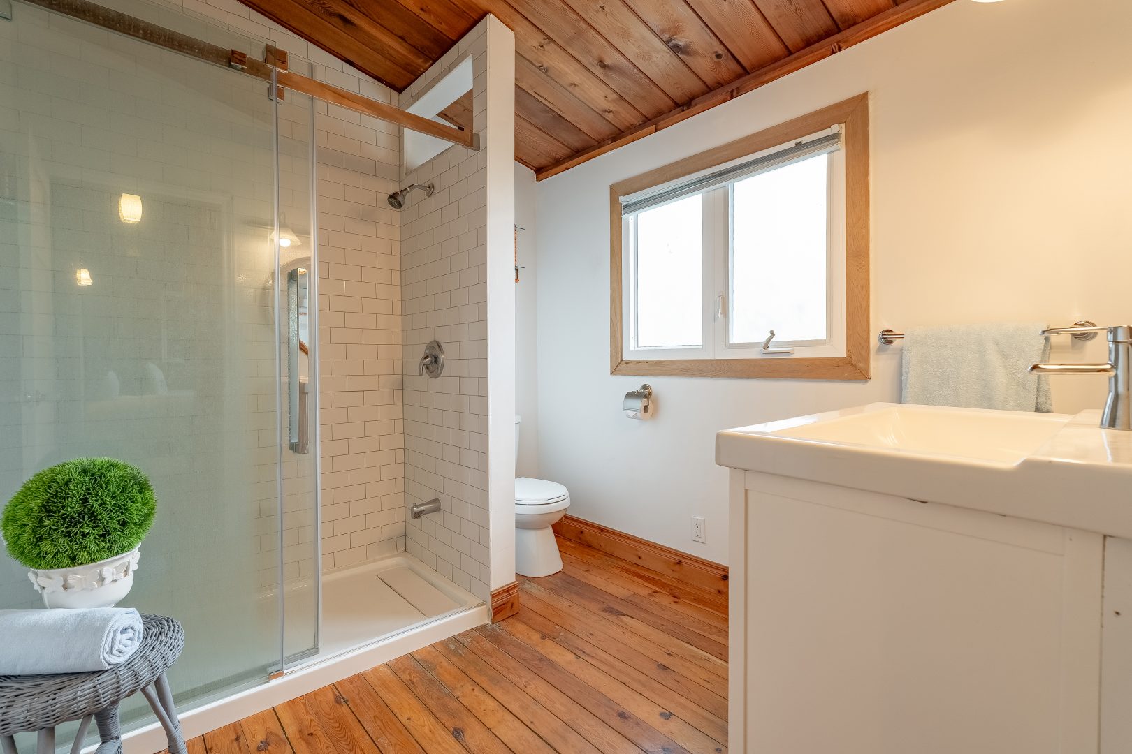 A glass walk-in shower faces a white vanity in a white and wood-clad bathroom