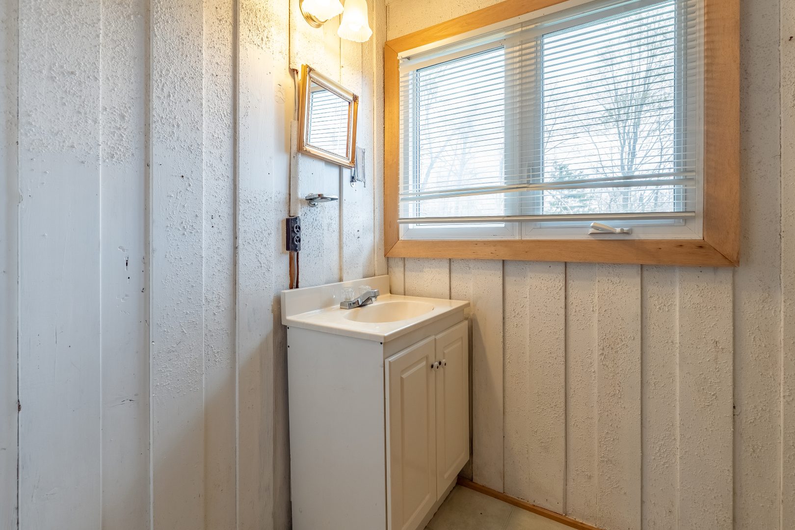A white vanity with a small mirror in a white paneled bathroom