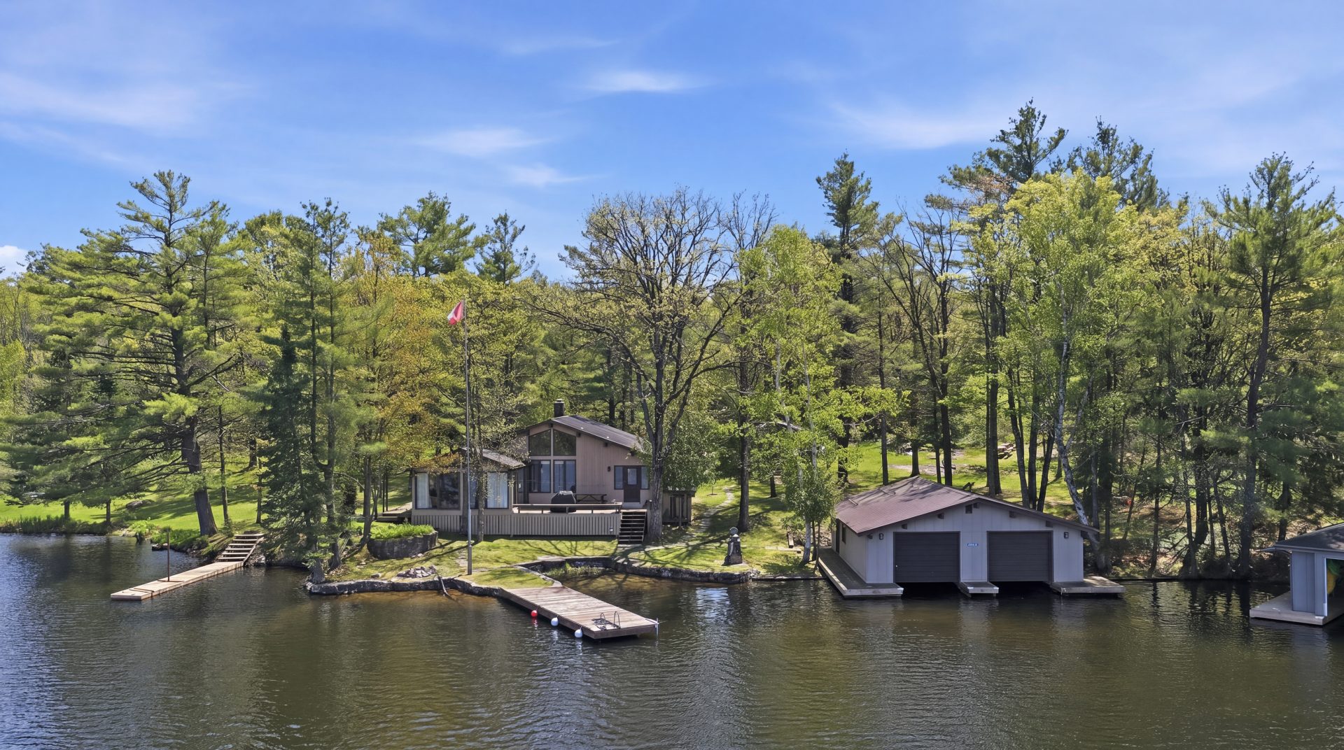 A beige wood cottage with a matching boathouse and dock on a forested shoreline