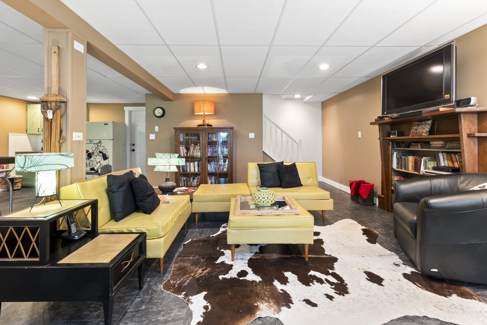A light yellow L-shaped couch in a basement with a cow hide blanket