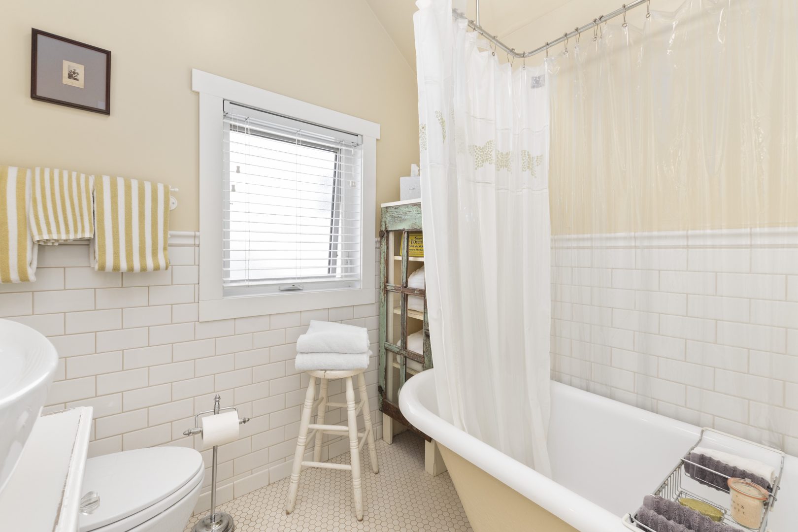 A cream bathroom with lower clapboard paneling and a white clawfoot tub