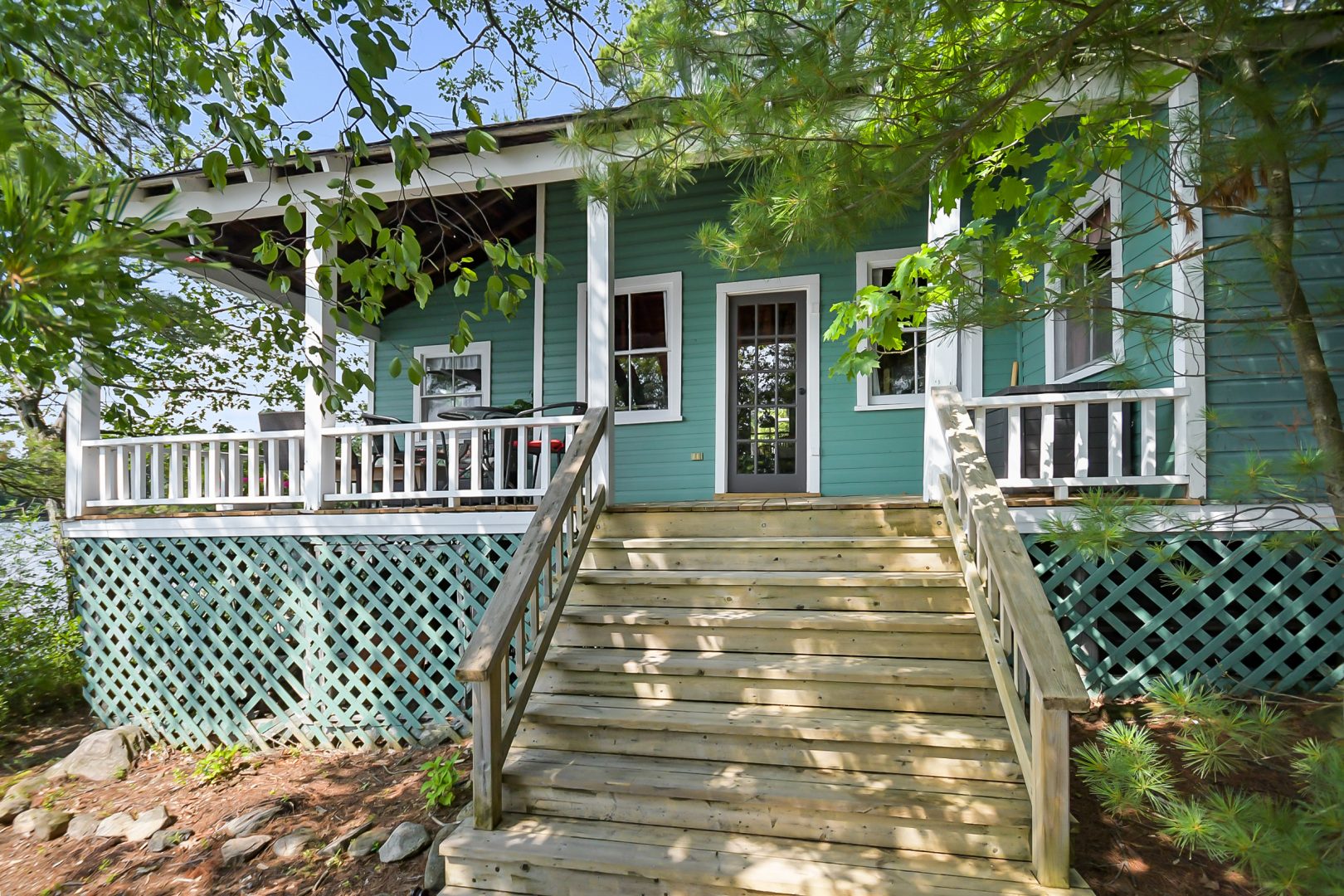 A teal clapboard cottage with white trim tucked between trees