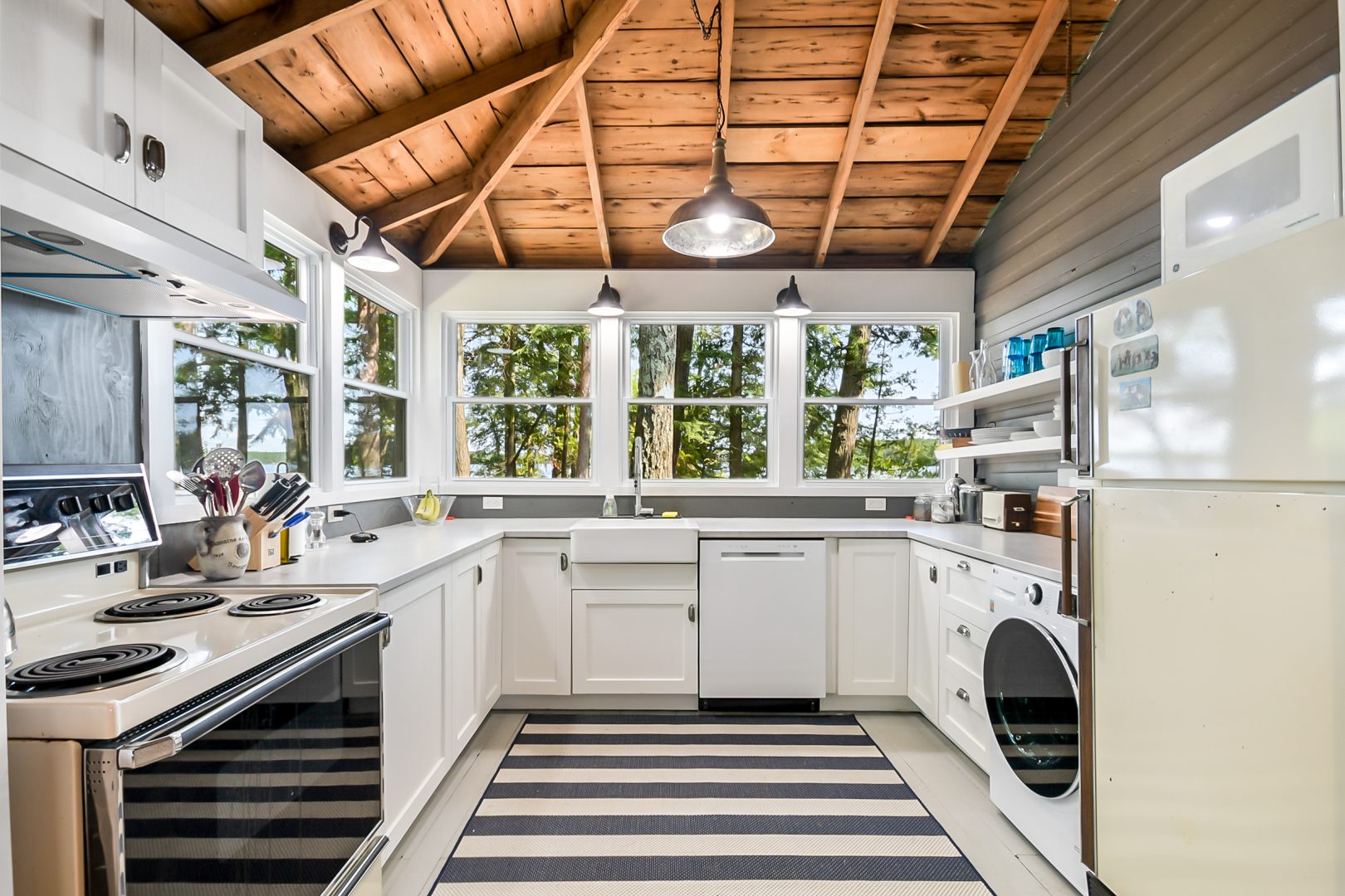 A bright white kitchen with a striped carpet and wood-paneled ceiling