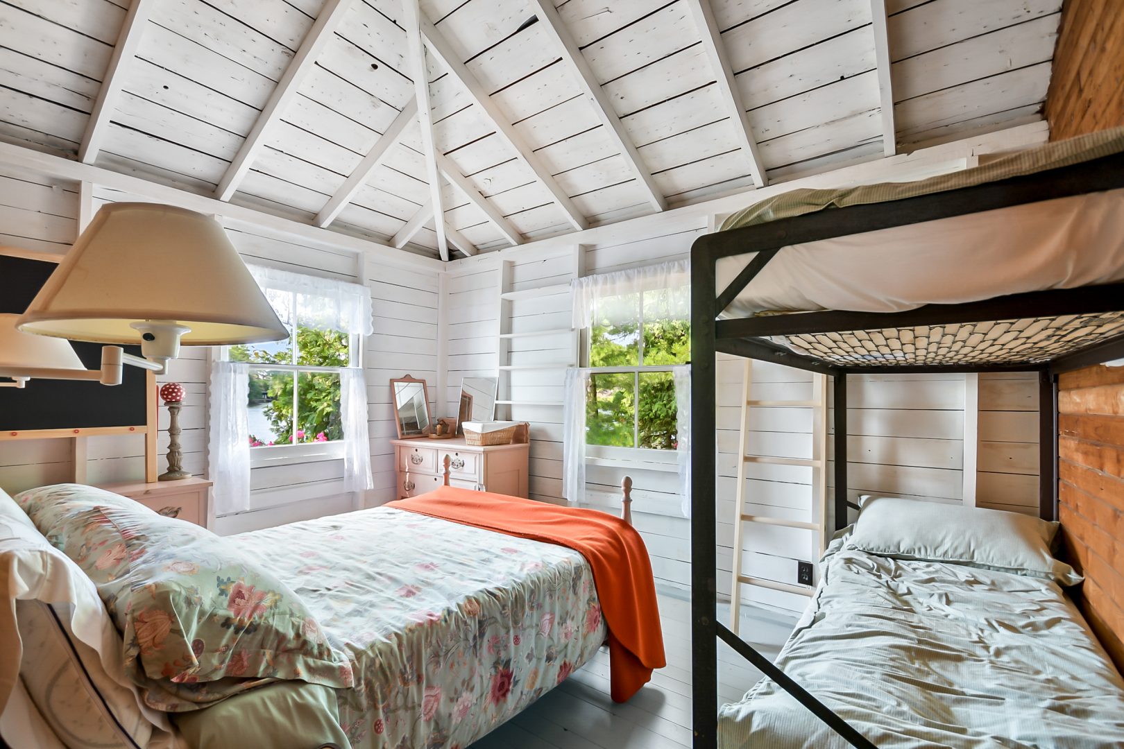A white patterned bed with a red throw next to bunk beds in a white bedroom