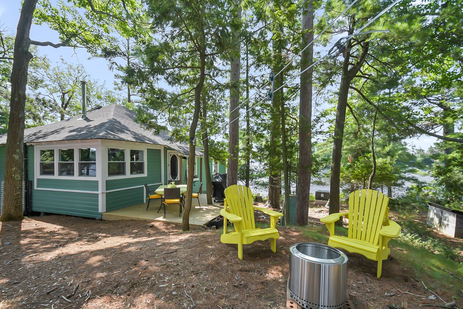 Yellow Muskoka chairs facing a fire pit on the cottage property next to a teal cottage.