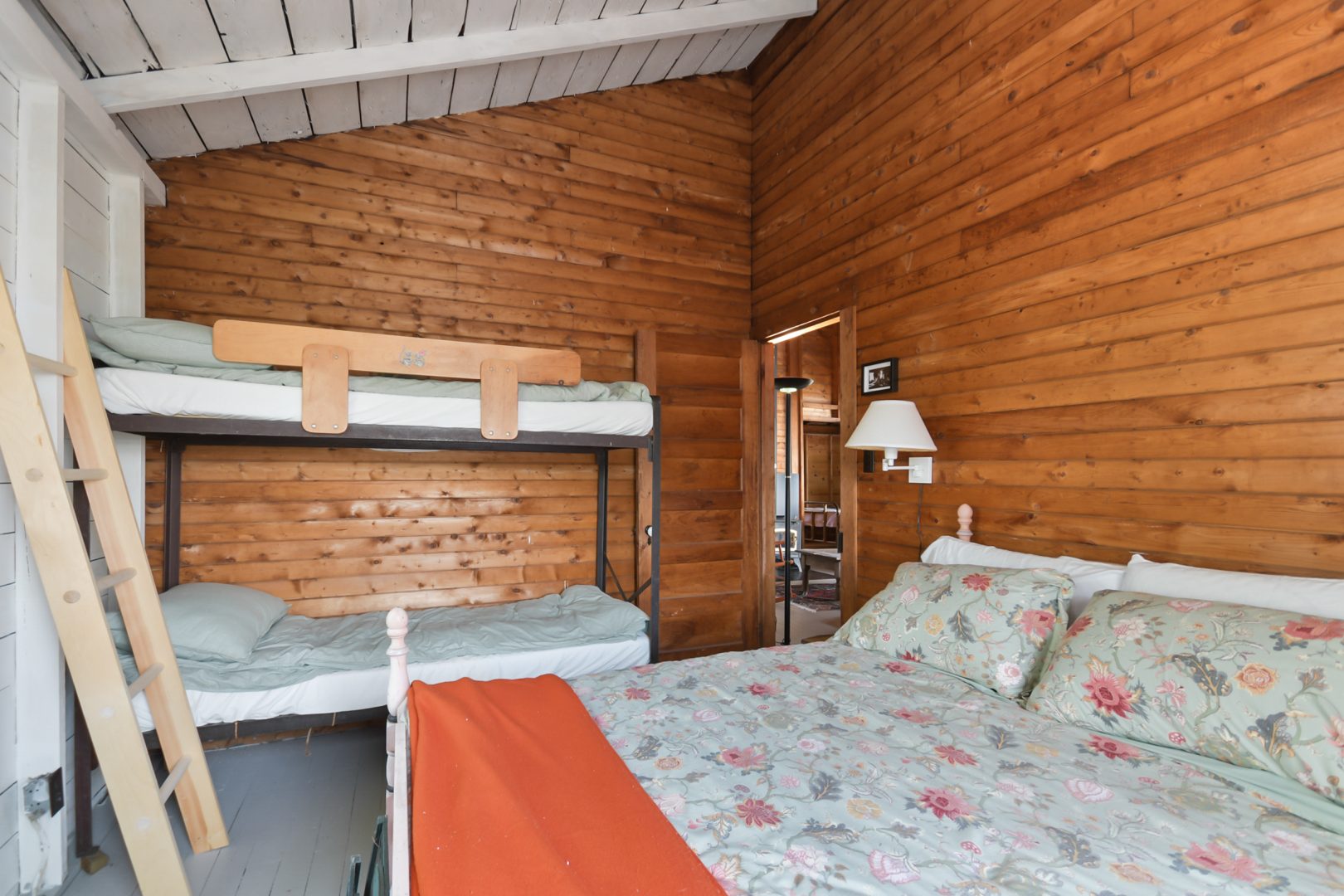 A patterned bed with an orange throw blanket in a wood-paneled room