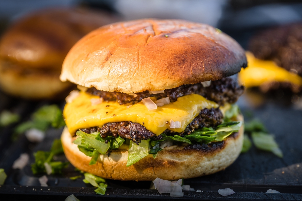 close-up of homemade double smash burger with cheese, lettuce, onion and dressing lying on a cutting board