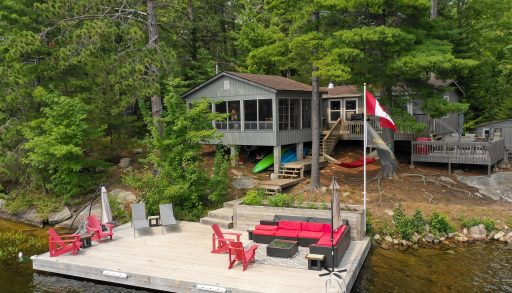 A grey cottage with multi-level decks on a forested property with a large dock