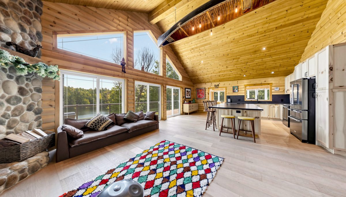 A living room with cathedral ceilings and floor-to-ceiling windows. A couch faces away from the windows adjacent to the dining table