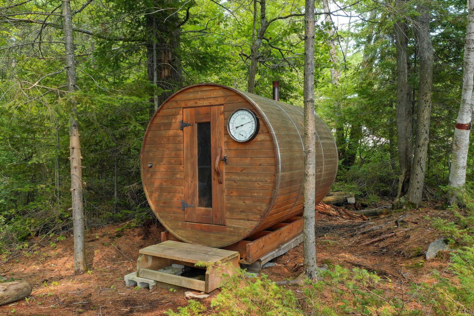 A barrel sauna tucked amongst green trees