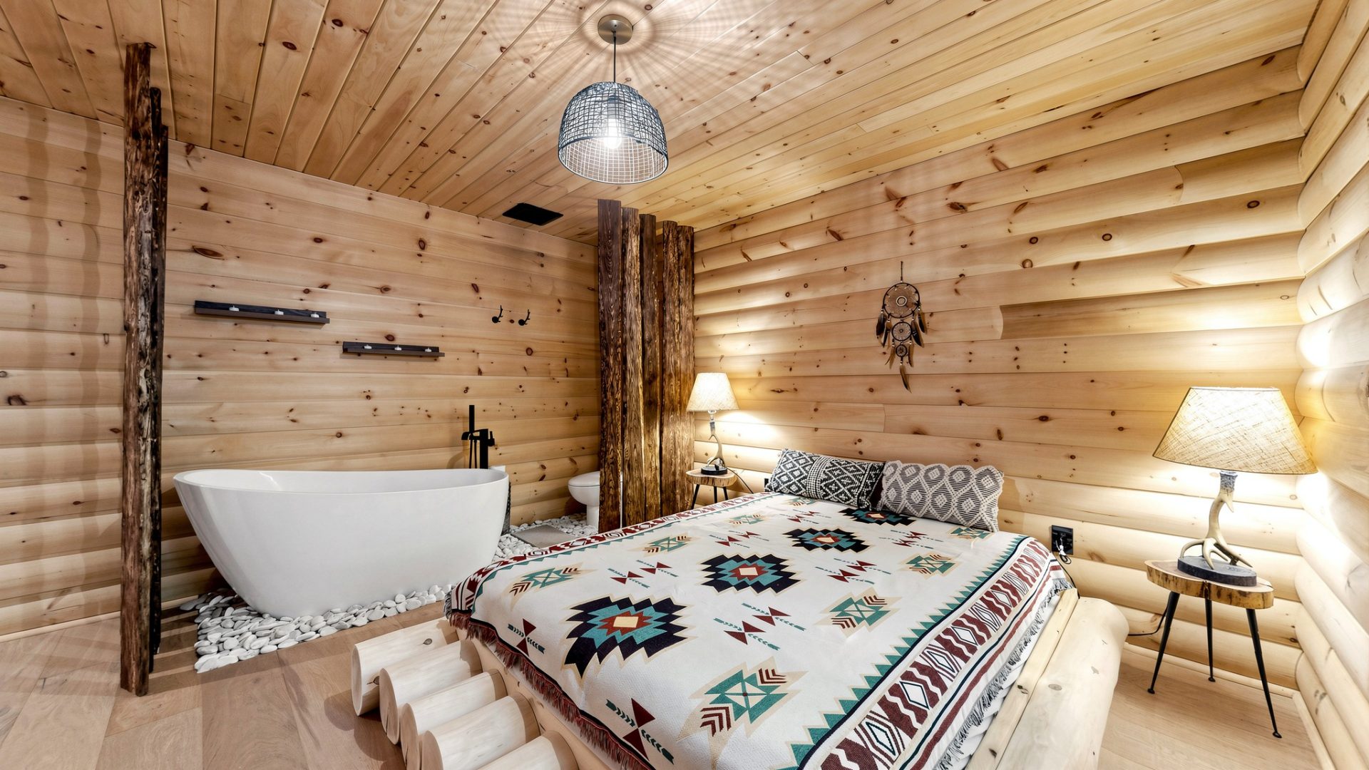 A bed with a boho-print bedspread sits on a wood slat. Next to it is a soaker tub and toilet partially hidden from view by a wood partition