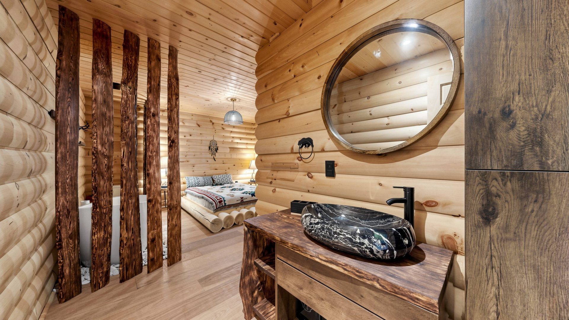 A round stone sink on a wood vanity in a wood-clad room. Tucked around the corner is a low-set bed.