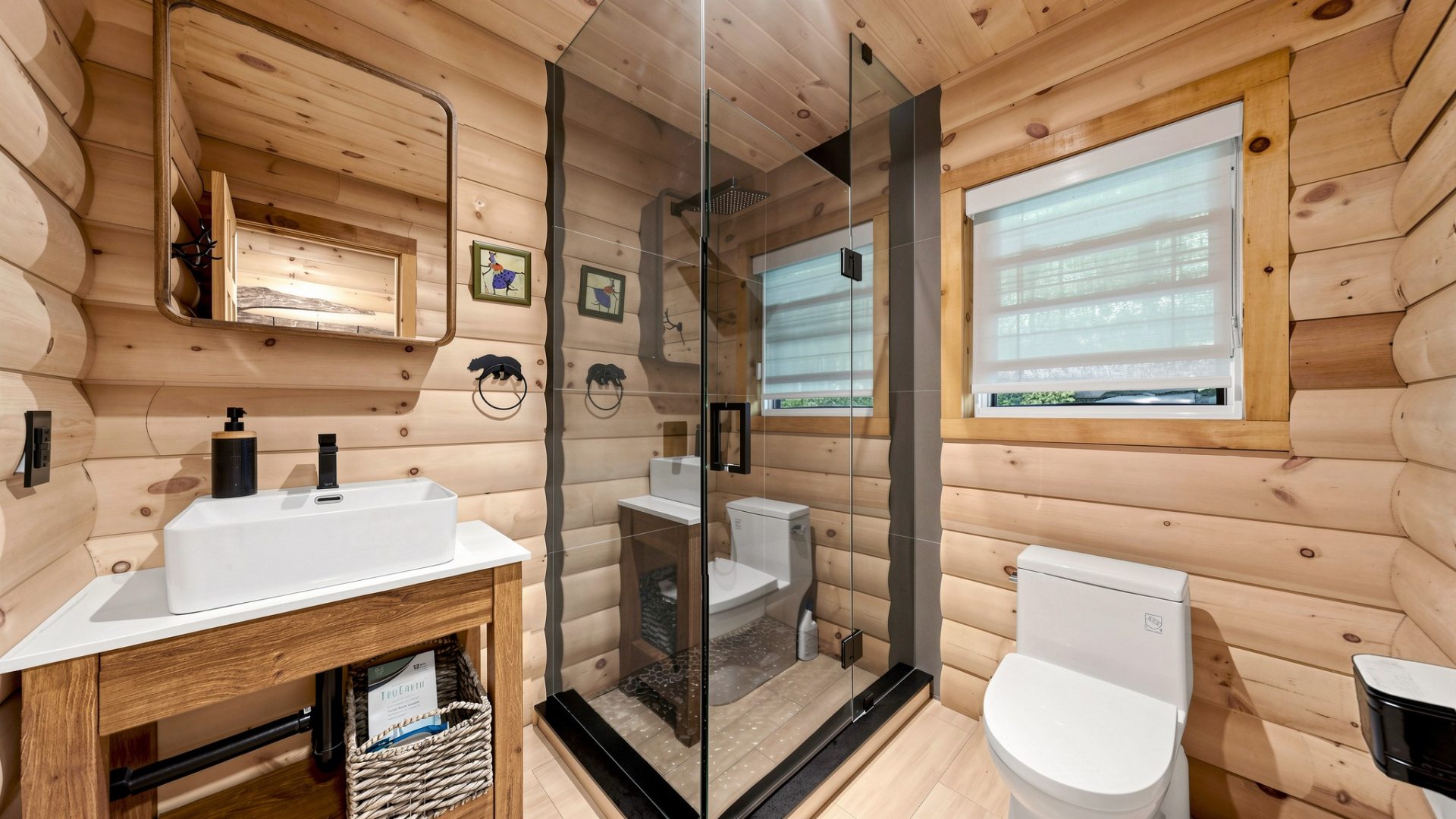 A glass walk-in shower next to a wood vanity and white toilet in a wood-clad bathroom