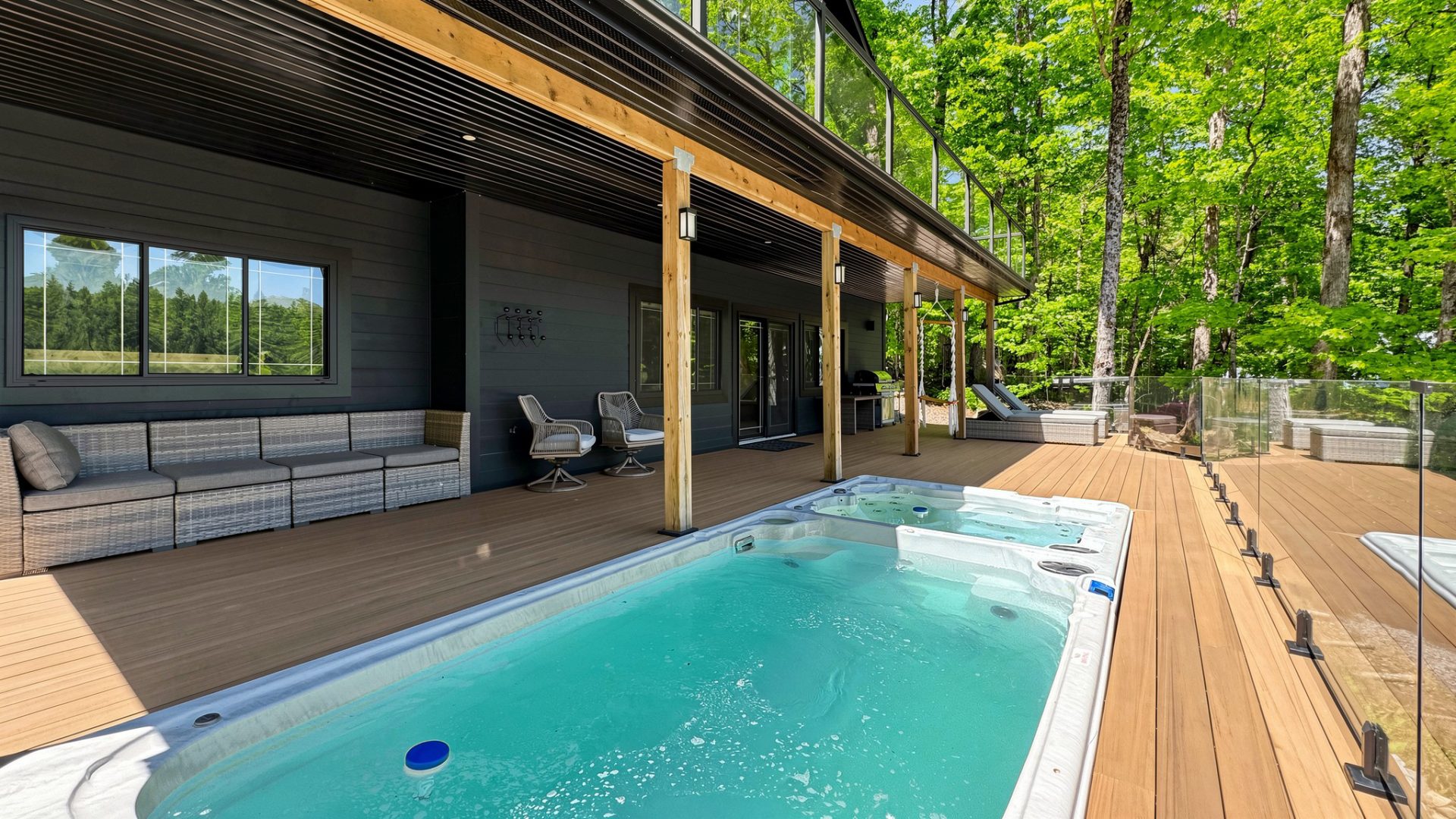 A blue pool on a light wood deck next to a black cottage