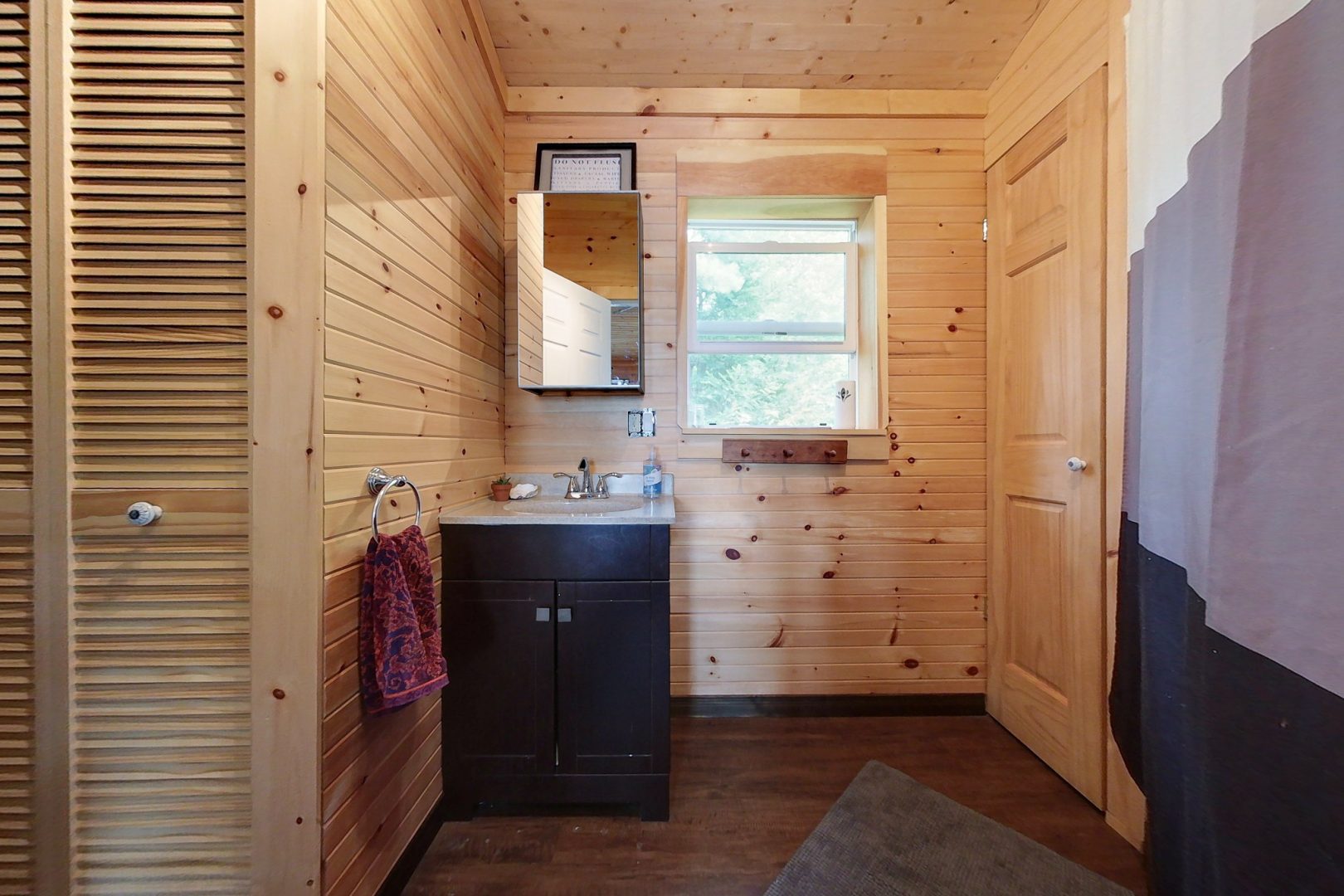 A wood-paneled bathroom with a small dark wood vanity and mirror