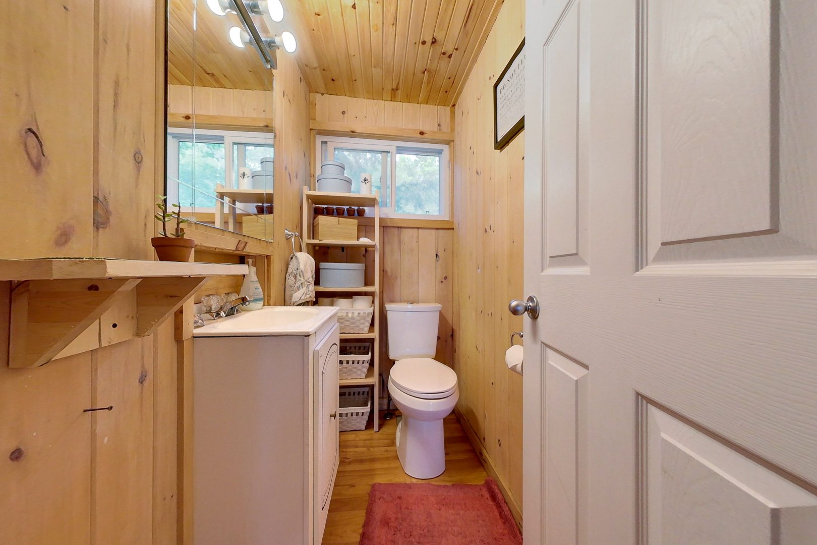 A narrow light wood-paneled bathroom with a white vanity