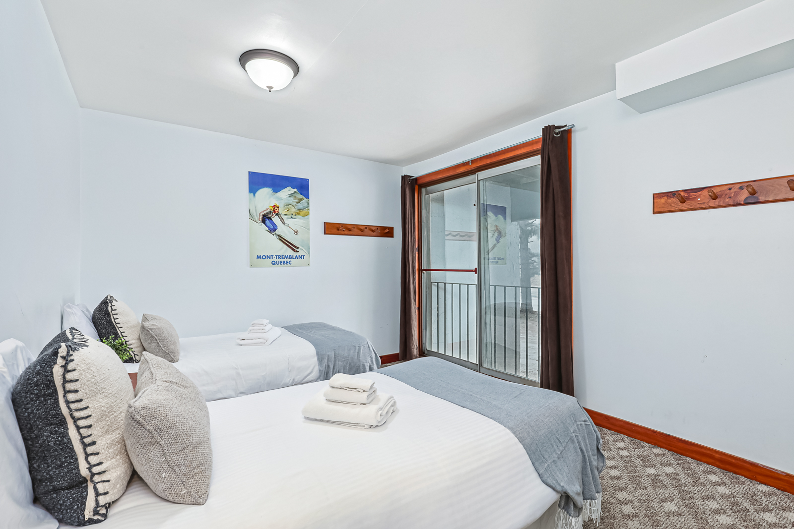 Two white beds with grey throw blankets face a glass door