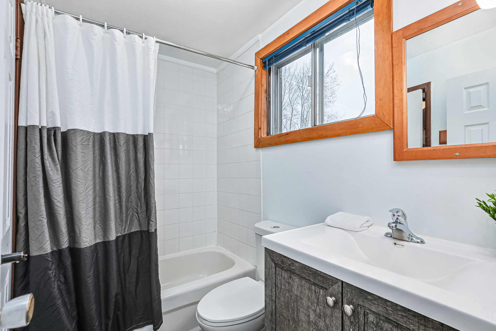 A white bathroom with a white tub and grey shower curtain.