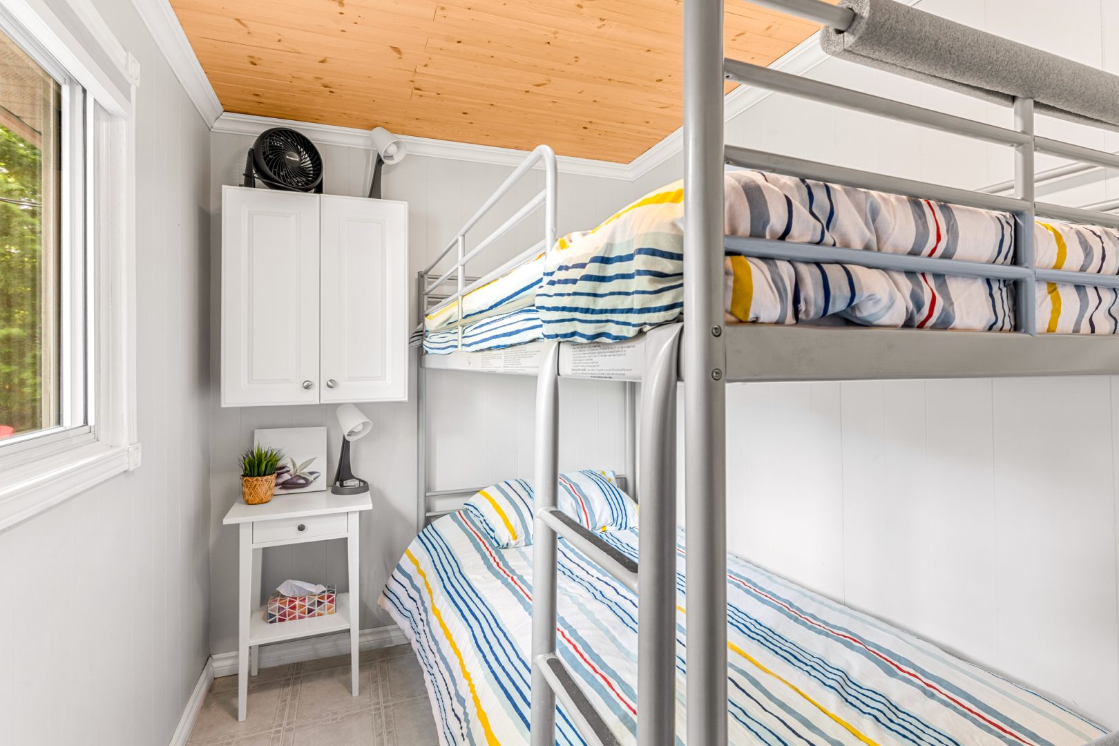 A metal bunk bed with striped bedding in a white bedroom