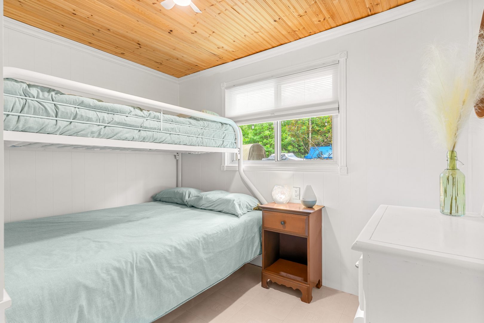 White bunk beds with light blue covers in a white bedroom with wood ceilings