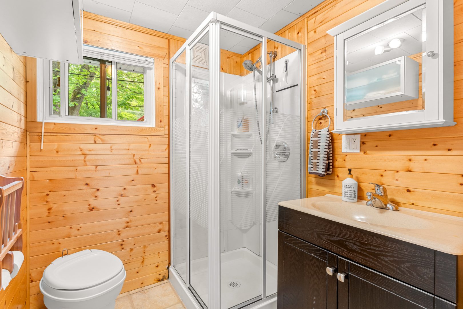 A wood-clad bathroom with a white walk-in shower next to a dark wood vanity